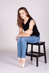 En Pointe resting on stool legs together sad expression en pointe Beautiful teen girl sitting straight looking at the camera with an sad or hurtful look, holding arm. Metaphor for pain.