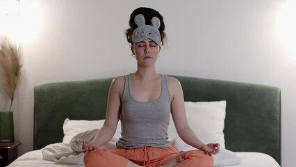 Young Caucasian woman meditates sitting on bed. Evening yoga before going to bed. Rest and relaxation