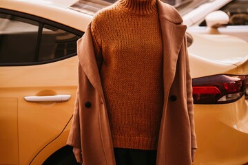 Female body in the orange warm knitting cozy sweater and long brown coat against the yellow taxi.....