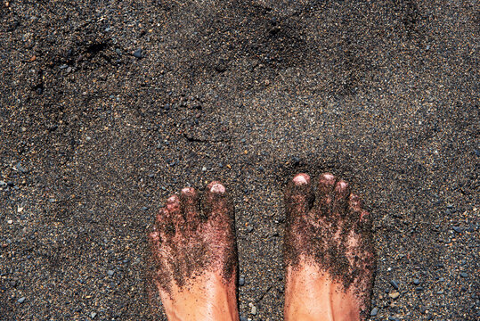 
Pies descalzos de un hombre en la playa cubierta de arena negra en la costa volc&aacute;nica de Fuerteventura en las Islas Canarias.