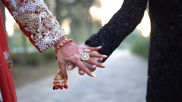 A delightful Pakistani couple captured in a heartwarming moment of togetherness, holding hands during their wedding photoshoot in a serene park setting.