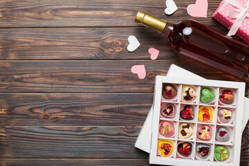 Bottle of red wine on colored background for Valentine Day with gift and chocolate. Heart shaped with gift box of chocolates top view with copy space