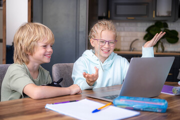 Online school class, siblings pupils boy and girl learning together remotely online at home, looking to laptop, speaking with teacher or tutor using internet