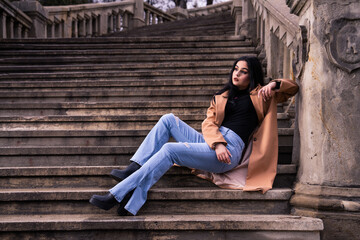 Fototapeta na wymiar a woman in a black top and jeans posing on steps with her legs crossed and her hand on her hip, fashion photoshoot
