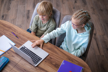 top view siblings pupils boy and girl learning together remotely online at home, looking to laptop,...