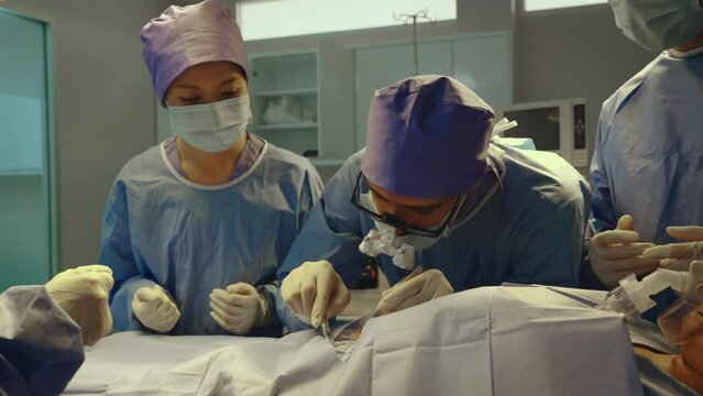 Doctor using tools at operation room. doctor took knife down cut chest in order urgently operate on patient, where everyone in room wears surgical gowns keep clean.