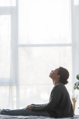 Side view of lonely multiracial woman with depression sitting on bed at home.