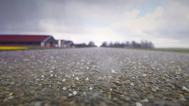 Hail falling on a country road in a rural landscape during a springtime storm. Slow motion clip.