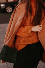 Female body in the orange warm knitting cozy sweater and long brown coat. Outdoor portrait in...