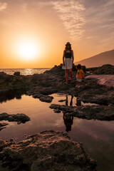 Mother and son at sunset on the beach of Tacoron on El Hierro, Canary Islands, vacation concept, orange sunset