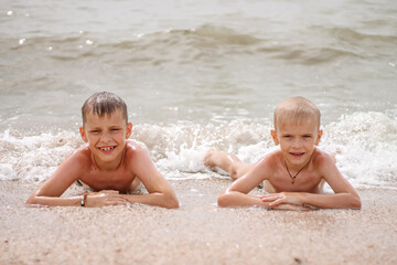 two brother boys are splashing in the sea spray and laughing