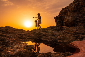 Silhouette of mother and son walking in the sunset on the beach of Tacoron in El Hierro, Canary...