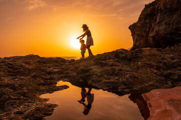 Silhouette of mother and son walking in the sunset on the beach of Tacoron in El Hierro, Canary Islands, orange sunset, walking along the sea pointing the path