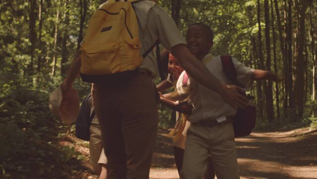 Slowmo of happy multiethnic cub scouts running towards their scout leader along forest trail on sunny day