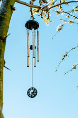 Wind chime with zen symbolism hanging on tree in blossom with sky background