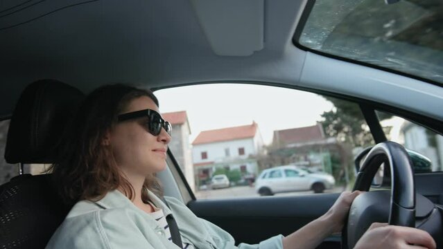 A young Caucasian woman in sunglasses driving a car, view from the inside of the car.