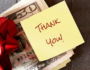 Money and red ribbon on gray background with note written THANK YOU, concept of money gift -  bonus or incentive for business staff , to show appreciation