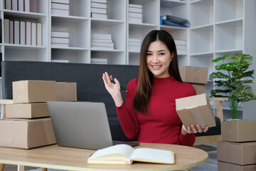 Asian business woman leaning on the sofa use laptop computer checking customer order online shipping boxes at home. Starting Small business entrepreneur SME. Online business, Work at home concept.