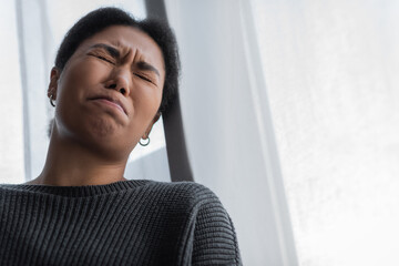 Low angle view of young multiracial woman with depression crying at home.