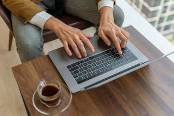 Close up of a businessman hand over the keyboard of a laptop on a desk with a cup of coffee