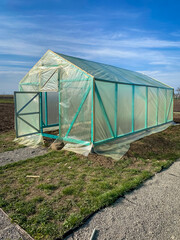 A wooden greenhouse is being built, which is covered with a transparent film. The wooden frame is painted in turquoise color.