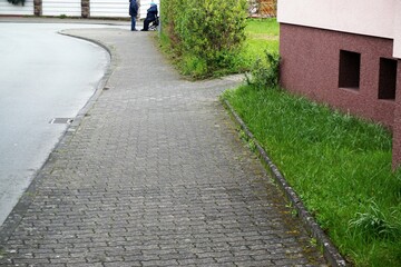 Gehweg mit alten Pflastersteinen zwischen Straße und pinkem Haus vor altem Ehepaar am Morgen im Frühling