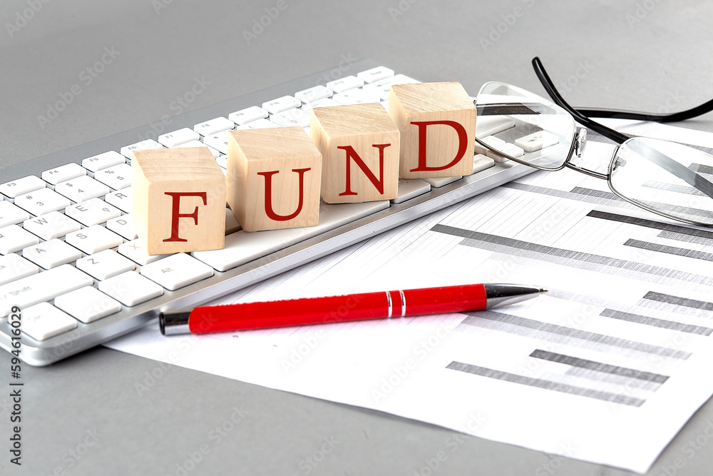 Poster fund written on a wooden cube on the keyboard with chart on grey background