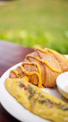 breakfast dish with savory croissant with Omelette, served with fresh healthy salad on a white plate and dipping sauce
