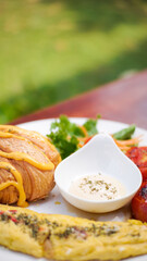 breakfast dish with savory croissant with Omelette, served with fresh healthy salad on a white plate and dipping sauce
