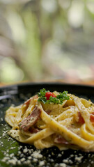 creamy spaghetti carbonara with grated parmesan, sausages and smoke beef on black plate