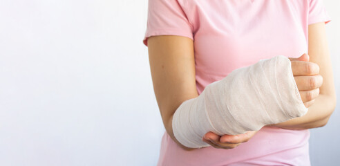 Close-up of a woman's broken arm in a cast. The girl holds a bent arm against the background of a pink t-shirt. Banner, copy space. Insurance medicine concept.