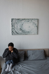 Young multiracial woman with depression sitting on bed at home.