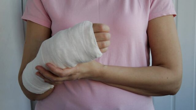 A woman stretches her fingers on a broken arm in a plaster cast and sways in pain. Health insurance concept.