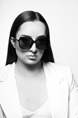 Fashion and business concept. Young and beautiful woman with long dark hair studio portrait. Model wearing white suit and sunglasses. Black and white image