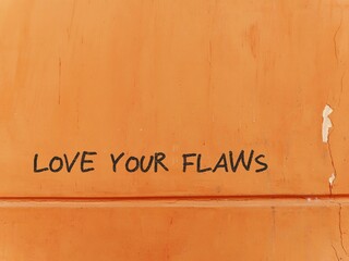 Old grunge orange wall with red text LOVE YOUR FLAWS, concept of positive self talk, learning self...