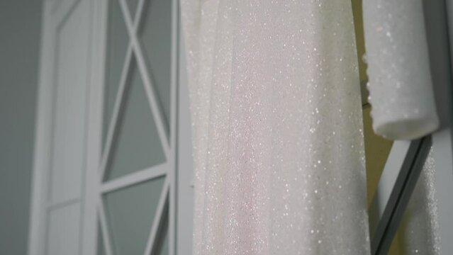 A beautiful white wedding dress hangs on a hanger on the wardrobe in the bedroom. Morning of the bride, wedding day. Women's fashionable clothes for the holiday.