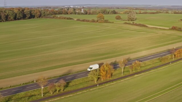 A drone accompanies transporter on a country road, from village to village, along green fields. Location: Germany