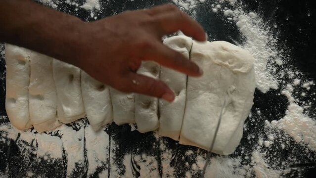 Top view of a man cutting fresh white dough on a table with flour