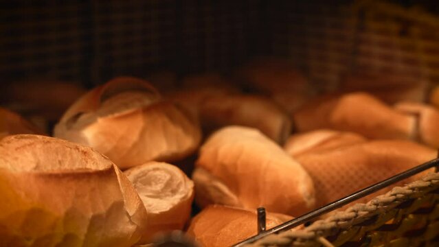 Closeup of a male picking a fresh bread bakery on a basket by bread tongs