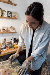 Vertical shot of a woman creating artwork in an art studio interior lit by natural light