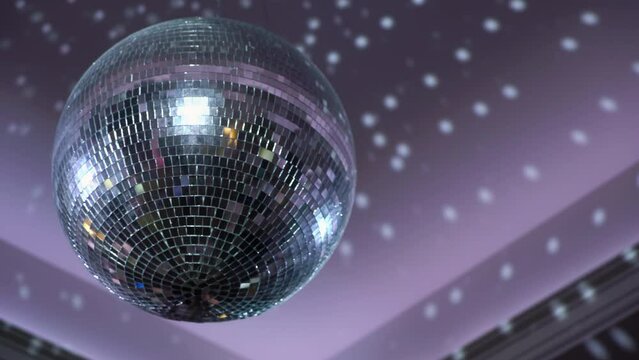 Silver mirror disco ball suspended from the ceiling rotates quickly, light spot rays and glare. White stage light at a concert hall, club, party or disco. Illumination and atmosphere.