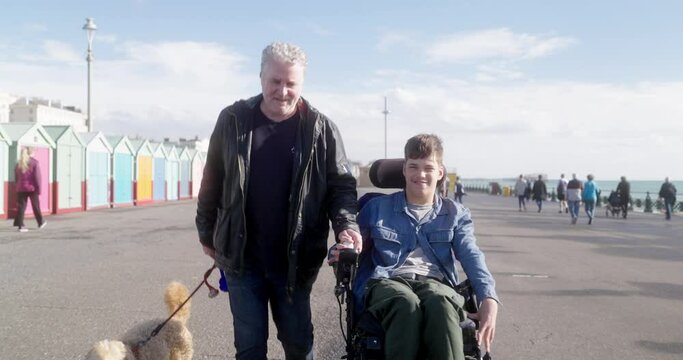 MS DS Father and disabled son walking with dog on promenade