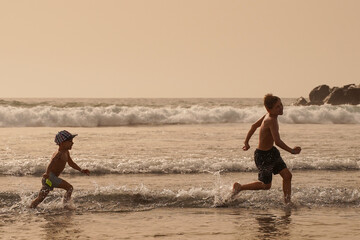 Fototapeta premium Children have fun running on the beach by the water. The brothers are chasing each other