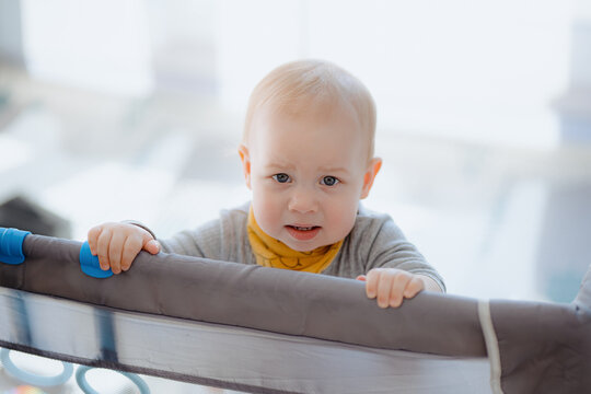 A boy toddler crying in a playpen. Tearful child standing in playpen. baby looking from playpen with a tears in his eyes indoors in the nursery