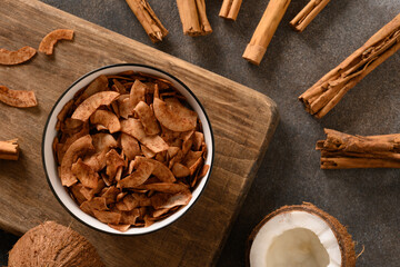Coconut chips with cinnamon in bowl on brown background, home drying. Vegan and sugar free dessert....
