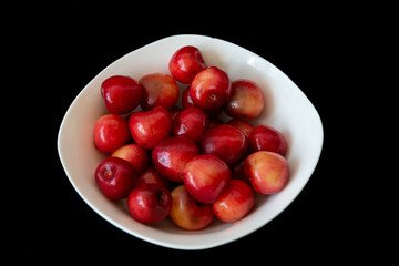 Fresh ripe cherries in a white plate on a black background. Vegetarian breakfast. Healthy food.