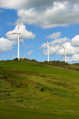 wind turbines among the green hill pastures in the clouds and wind of spring