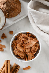 Coconut chips with cinnamon in glass jar on white background, home drying. Vegan and sugar free dessert. Vertical format. Sri lankan local snack. Top view.