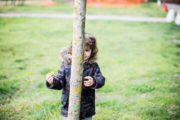 child plays behind a tree, plays hide and seek and peek-a-boo, laughing and very amused and happy