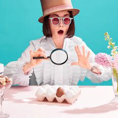 Shocked woman in sunglasses and cylinder hat emotionally looking in magnifying glass at chocolate...